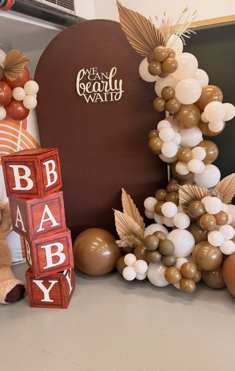 Teddy bear themed baby shower backdrop with neutral balloon garland and dried palm accents